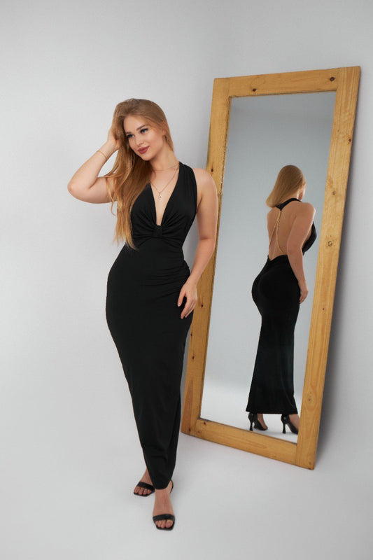 Woman in a black dress standing next to a full-length mirror on a gray background