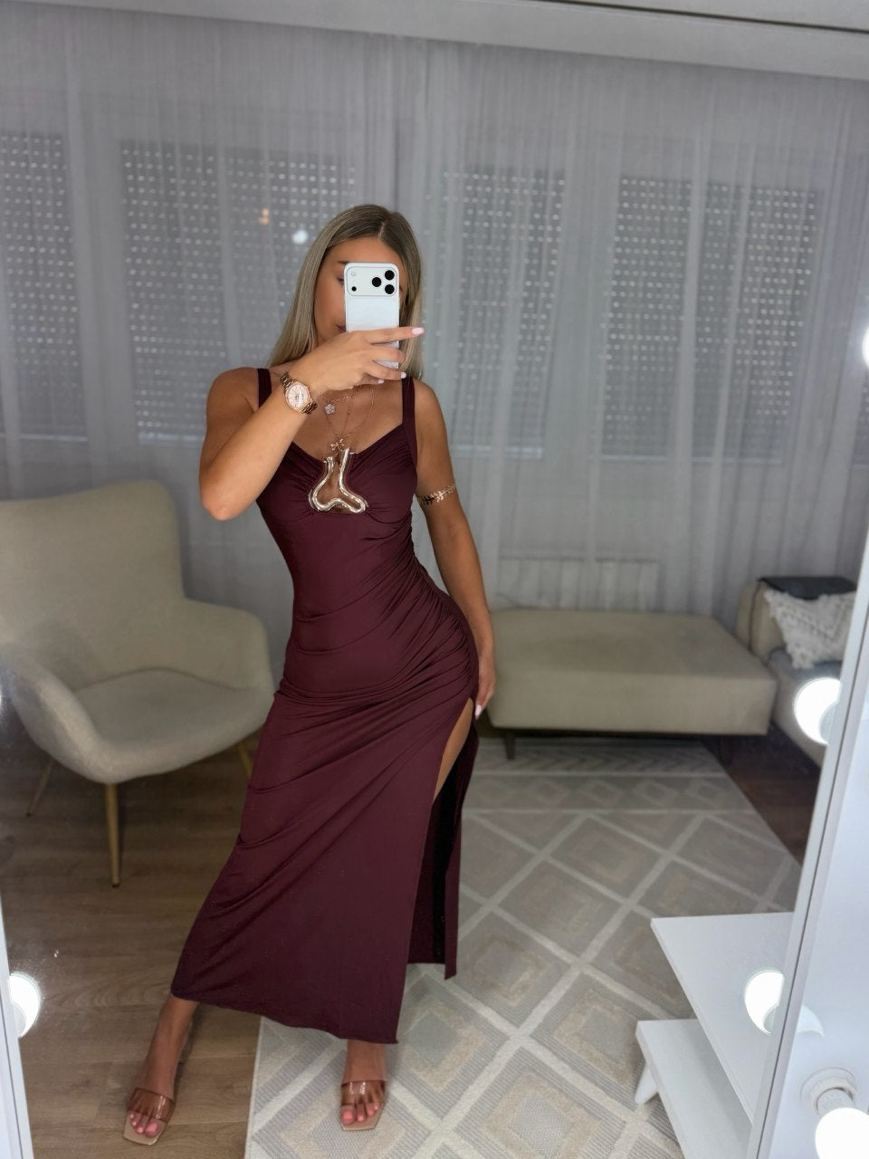 Captivate the room in this stunning burgundy maxi dress, designed to command attention at any upscale evening event. Crafted from a form-fitting, ruched fabric that hugs your curves, this dress features a striking sweetheart neckline accentuated by a bold metallic gold abstract hardware piece at the center. The sleek silhouette flows down into a dramatic floor-length finish with a high side slit, offering both glamour and effortless movement. Pair this showstopper with metallic statement accessories and you